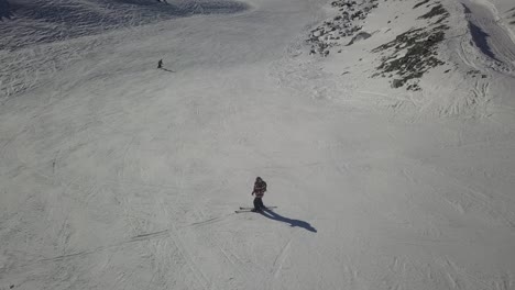 Skier-stopped-amidst-downhill-ski-track-overtaken-by-skiers-gliding-down-in-Val-Thorens,-French-Alps---Aerial-static-shot