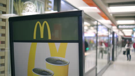 Nahansicht-Des-Schildes-Vor-McDonald&#39;s,-Während-Die-Leute-Hinterhergehen,-Slomo