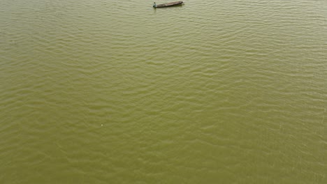 Un-Hombre-Sentado-En-La-Parte-Delantera-De-Su-Bote-Mientras-Tira-De-Su-Red-Mientras-El-Dron-Se-Va-Volando,-Muak-Klek,-Saraburi,-Tailandia