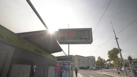 Tramway-station-with-people-walking-and-billboard-with-arrival-times,-Looking-up-pan-left-shot