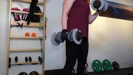 Beautiful-young-brunette-performing-biceps-curl-training-arms-in-her-home-gym---Strong-smiling-woman