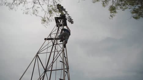 Hombre-Escalando-Un-Molino-De-Viento-En-Una-Granja-En-El-Norte-De-México,-Tiro-Ancho-De-ángulo-Bajo