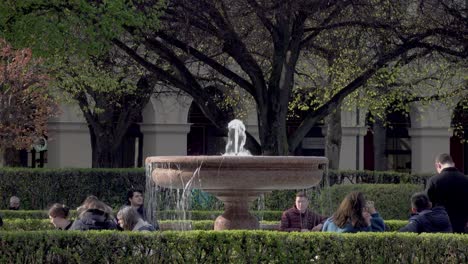 People-sitting-around-a-fountain-at-the-Hofgarten-in-Munich,-Bavaria,-Germany-enjoying-a-nice-spring-day