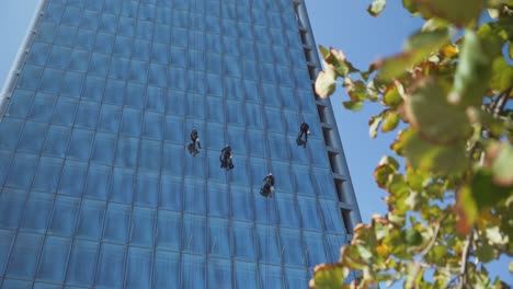 Nahaufnahme-Von-Vier-Fensterputzern,-Die-Tagsüber-An-Einer-Glasfassade-Eines-Modernen-Wolkenkratzers-Hängen-Und-Schwingen,-Santiago,-Chile