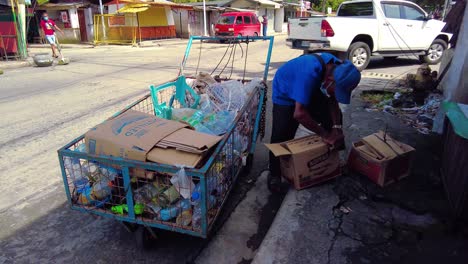 Un-Anciano-Rebuscando-Botellas-De-Plástico,-Cajas-De-Papel-Y-Chatarra-Al-Lado-De-La-Calle-Bajo-El-Sol