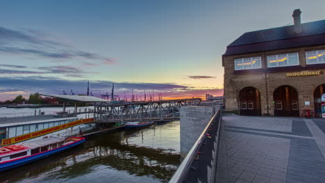 Tiro-De-Hiperlapso-Que-Muestra-El-Puerto-De-Hamburgo-Con-Torre-Y-Turista-Caminando-En-El-Puerto-Durante-La-Puesta-De-Sol,-Alemania