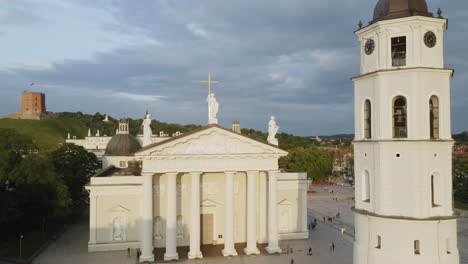 Aérea:-Toma-De-Pedestal-De-La-Catedral-De-Vilnius-Y-El-Campanario-Con-El-Cielo-Azul-De-Fondo-Y-Gente-Caminando-Por-El-Suelo