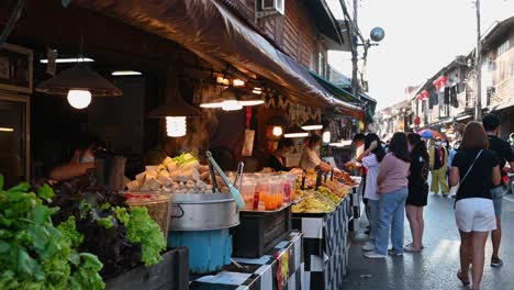 Vendors-preparing-food-to-give-to-the-tourists-as-people-walk-by-on-the-street,-Walking-Street,-Chiang-Khan,-Loei-in-Thailand