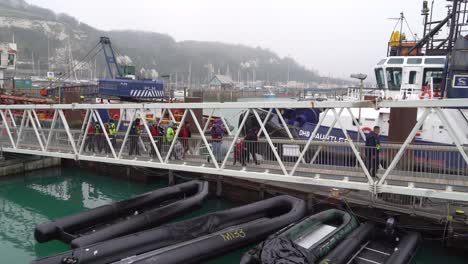 Refugees-and-migrants-walk-up-the-walkway-past-their-discarded-inflatable-boats-in-the-port-of-Dover,-UK