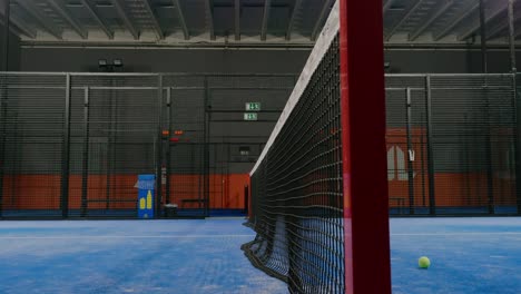 Padel-Ball-Flying-Over-Net-in-Interior-Court---Handheld-Medium-Close-Up