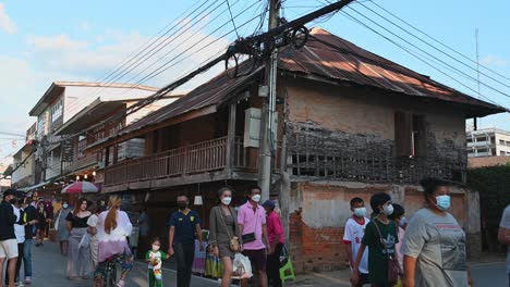 People-walking-towards-the-right-and-a-woman-leaning-against-the-brick-wall-taking-selfies-with-another,-Walking-Street,-Chiang-Khan,-Loei-in-Thailand