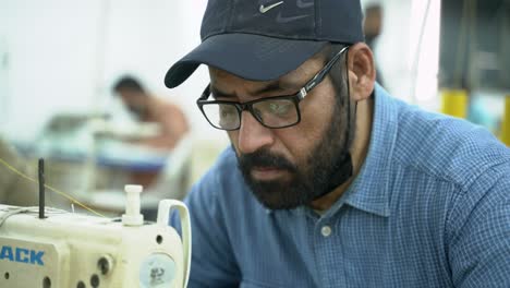 Retrato-De-Un-Hombre-Cosiendo-En-Una-Fábrica-De-Ropa-Industrial,-Pakistán