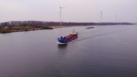 Aerial-View-Of-Wilson-Mosel-Cargo-Ship-Approaching-Along-Oude-Maas-With-Still-Wind-Turbines-In-Background-In-Barendrecht