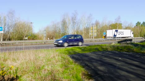 Una-Filmación-Estacionaria-De-Camiones-Y-Vehículos-En-Movimiento-Rápido-A-Lo-Largo-De-La-Carretera