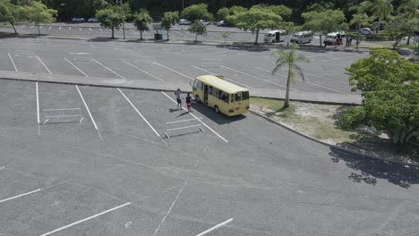 Vista-Aérea-De-Los-Turistas-Que-Salen-Del-Autobús-En-El-Estacionamiento-De-Las-Cataratas-Del-Río-Dunn,-Jamaica