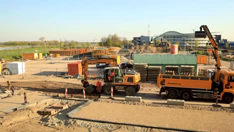 Time-lapse-of-machinery-clearing-asphalt-pieces-of-temporary-road-on-construction-site-gathered-by-a-digger-putting-it-on-a-truck-for-transport