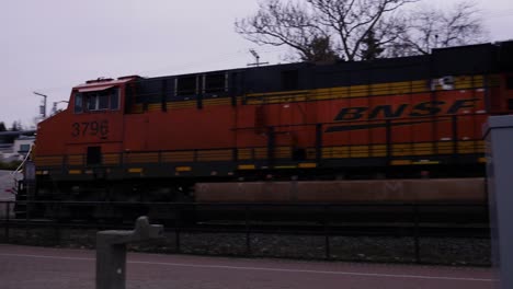 A-train-locomotive-engine-tracking-across-a-pedestrian-crossway-at-a-park-with-red-lights-flashing-and-people-waiting