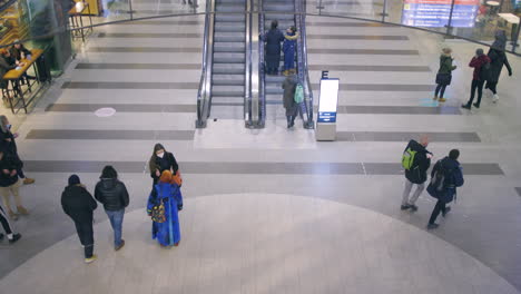 People-with-face-masks-walk-by-escalators-in-mall,-slomo-from-above