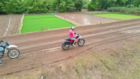 Los-Motociclistas-Conducen-Por-Un-Camino-De-Tierra-A-Través-De-Exuberantes-Campos-En-Camboya