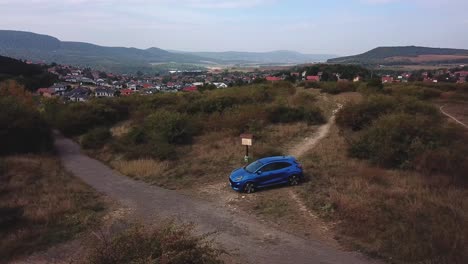 Vista-Aérea-De-Un-Puma-Ford-Azul-Estacionado-Junto-A-Un-Cruce-De-Caminos-Del-País,-En-La-Cima-De-Una-Colina