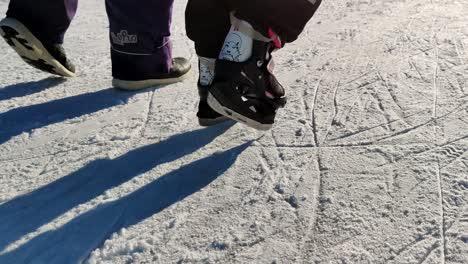 Toddler-girl-trying-to-learn-ice-skating---help-from-adult-mother,-stumbling-ahead-on-the-ice