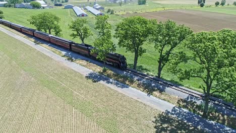 Una-Vista-De-Drones-De-Una-Locomotora-De-Vapor-Con-Vagones-De-Pasajeros-Acercándose-Al-Campo-En-Un-Hermoso-Día-De-Verano