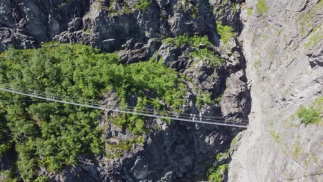 A-Través-Del-Puente-Ferrata-Que-Cruza-El-Cañón-De-La-Garganta-Profunda-En-Loen-Noruega---Peligroso-Puente-Colgante-En-Ruta-A-La-Montaña-Hoven---Antena-Con-Una-Persona-Caminando-En-El-Puente-Al-Comienzo-Del-Clip