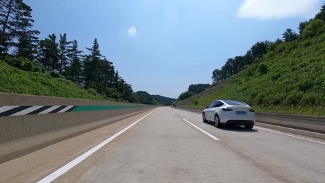 Sonniger-Tag-Auf-Der-Straße-Mit-Blick-Auf-Ein-Weißes-Tesla-Modell-Mit-Drei-Fahrenden-Autos