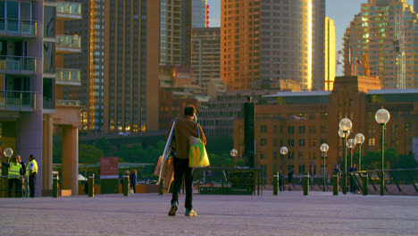 Persona-Con-Bolsas-De-Compras-Y-Lienzos-Caminando-Por-La-Calle-Al-Atardecer-En-Sydney,-Australia