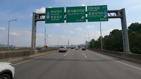 Punto-De-Vista-Del-Conductor-En-La-Carretera-Gangbyeonbuk-ro-Cerca-Del-Río-Han,-Torre-Lotte-En-El-Fondo-Seúl,-Corea,-27-De-Junio-De-2021-Día-De-Verano-Nublado