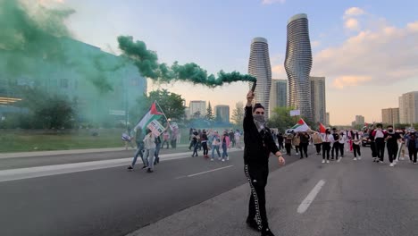 Ein-Demonstrant-Hielt-Eine-Grüne-Rauchbombe-Für-Eine-Pro-palästinensische-Kundgebung-In-Mississauga-In-Der-Hand,-Während-Die-Anderen-Im-Hintergrund-Ihre-Palästinensischen-Flaggen-Schwenkten,-Um-Auf-Den-Israelisch-palästinensischen-Konflikt-Aufmerksam-Zu-Machen