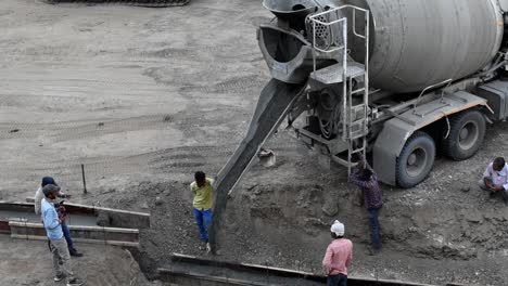 Workers-are-spreading-the-concrete-that-flows-and-pouring-from-a-cement-mixer-truck,-pouring-liquid-concrete-into-the-roadway-at-the-construction-site