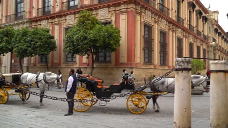 Panorámica-Sobre-Carruajes-De-Caballos-Estacionados-Y-Personas-En-Sevilla,-España