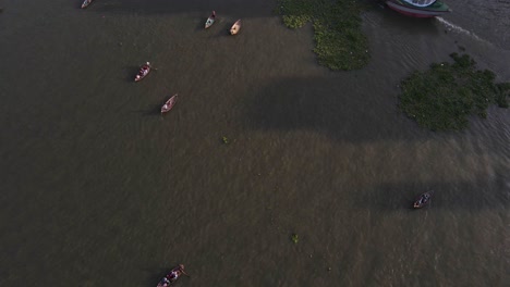 Vista-Aérea-De-Barcos-Y-Barcos-Que-Pasan-Para-Llegar-Al-Mar-Para-Pescar-Y-Una-Ciudad-Congestionada-Del-Viejo-Dhaka,-Bangladesh-En-El-Fondo-En-Una-Hermosa-Mañana