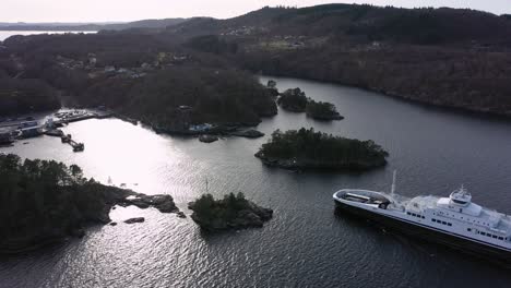 Torghatten-Nord-ferry-Flatoy-entering-narrow-passage-when-approaching-Sandvikvag-ferry-pier-along-E39-in-Norway---Static-erial-view-looking-down-at-ferry-from-a-distance