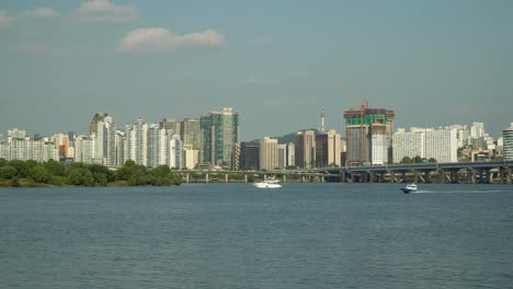 Barco-De-La-Policía-De-Hangang-O-Lancha-A-Motor-Acelerando-Rápidamente-O-Moviéndose-En-El-Río-Han-Con-El-Paisaje-Urbano-Urbano-De-Seúl,-Yate-A-La-Deriva,-Tráfico-En-La-Carretera-De-La-Autopista-Gangbyeon,-Puente-Mapodaegyo,-Torre-Namsan-De-Seúl