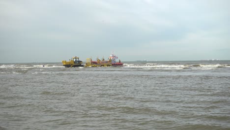 Hombre-En-Bote-Remando-Hacia-El-Bote-Salvavidas-Knrm-Conectado-Al-Tractor-En-El-Mar-Con-Olas-Embravecidas-Durante-La-Marea-Alta-En-Países-Bajos