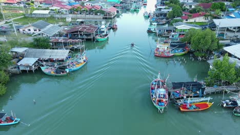 Aerial-footage-of-a-boat-moving-up-the-river-also-revealing-a-lovely-fishing-village,-people-doing-their-business