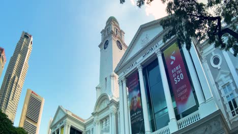 Facade-Of-Victoria-Theatre-And-Concert-Hall-With-Highrise-Buildings-Against-Blue-Sky-In-Central-Area-Of-Singapore