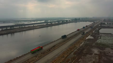 Aerial-View-Of-Lorries-And-Tankers-Travelling-Along-Road-Through-Water-logged-Agricultural-Land-In-Sindh