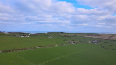 A-patchwork-of-green-fields,-a-rural-road-with-cars-and-blue-sky-with-white-clouds