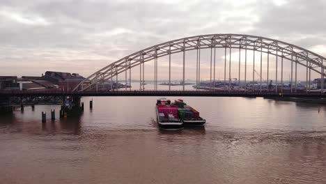 Vista-Aérea-Del-Buque-De-Carga-Excelsior-Emparejado-Con-Una-Barcaza-Que-Transporta-Contenedores-De-Carga-En-El-Río-Noord-Viajando-Bajo-Brug-Sobre-De-Noord