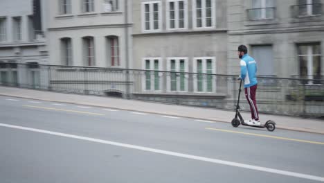 Blick-Auf-Einen-Jungen-Mann,-Der-An-Einem-Bewölkten-Tag-Auf-Einem-Zweirad-Vorbeifährt-Und-Auf-Einem-Elektroroller-Auf-Den-Straßen-Von-Freiburg-In-Der-Schweiz-Steht