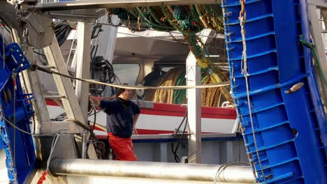 Marinero-Español-Con-Gorra-Viendo-El-Desenrollado-Automático-De-Redes-De-Pesca-Desde-Un-Barco-Industrial