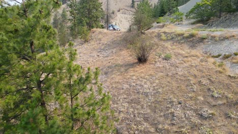 Caucasian-man-sitting-in-front-of-his-car-that-is-parked-at-the-side-of-a-dusty-mountain-road-in-the-Okanagan-region-in-British-Columbia