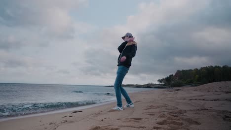 Young-Tall-Guy-With-Jacket-Throwing-Pebbles-To-The-Ocean-Then-Gets-Water-On-His-Feet---Static-Wide-Shot