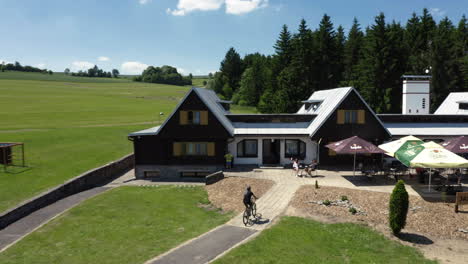 Ein-Mann-Tritt-Mit-Dem-Fahrrad-In-Die-Pedale-Und-Trifft-Familie-Und-Freunde-Auf-Der-Terrasse-Eines-Resorts,-Verfolgt-Aus-Der-Luft