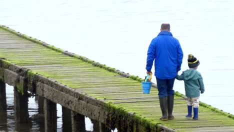 Father-holding-seaside-bucket-exploring-low-tide-UK-beach-walkway-with-his-inquisitive-son