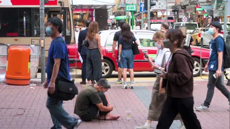 A-woman-puts-money-into-the-cup-of-a-beggar-as-pedestrians-pass-by-in-the-street-of-Hong-Kong