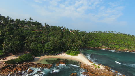 Dronie-Shot-Of-Two-Guys-Relaxing-On-Long-Chair-On-Sandy-Beach,-Sri-Lanka